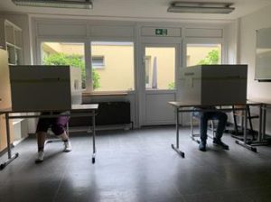 Wir mussten unsere Wahlbenachrichtung abgeben und haben unseren Stimmzettel bekommen. Dann durften wir in unsere Wahlkabine gehen.